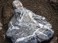 Grauer Stein mit chaotischem weißen Muster im Ufersand